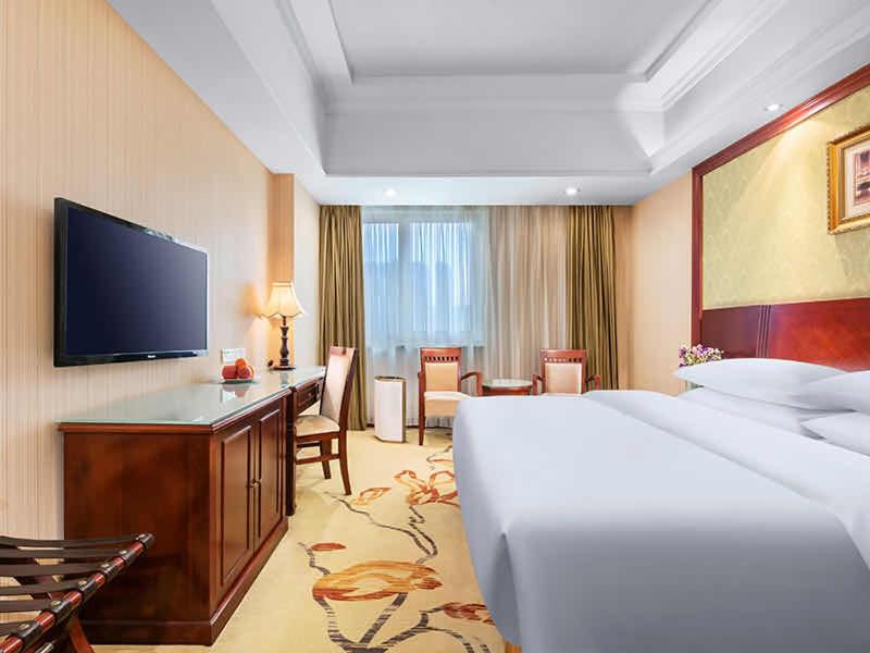 Vienna International Hotel - Hangzhou Wulin Square Branch في هانغتشو: غرفة فندقية بسرير وتلفزيون بشاشة مسطحة