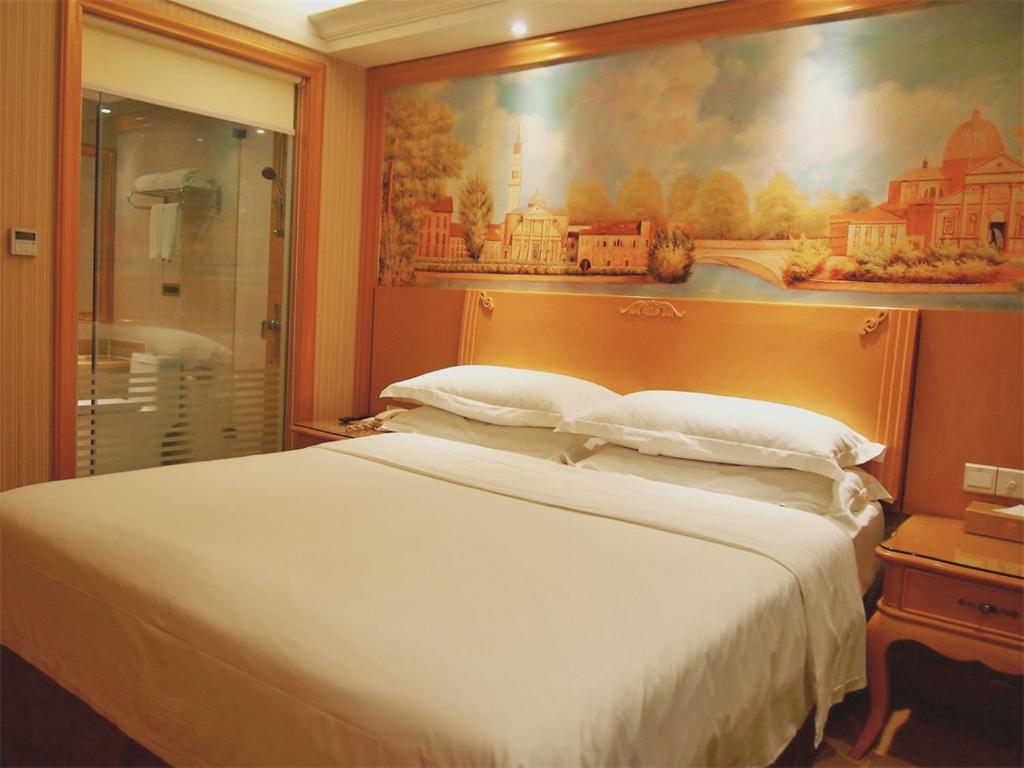 a bedroom with a large bed and a painting on the wall at Vienna Hotel Shenzhen Nanshan Yilida in Shenzhen