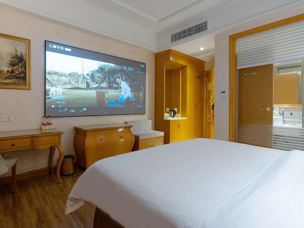 een slaapkamer met een grote flatscreen-tv aan de muur bij Vienna Hotel Guangzhou Beijing Road in Guangzhou