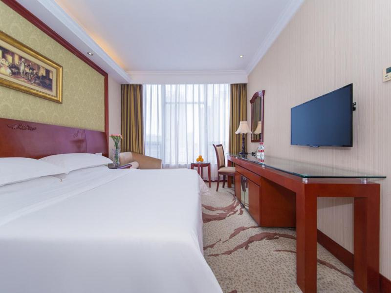 a hotel room with a bed and a desk with a television at Vienna International Hotel Xiangyang Railway Station in Xiangyang