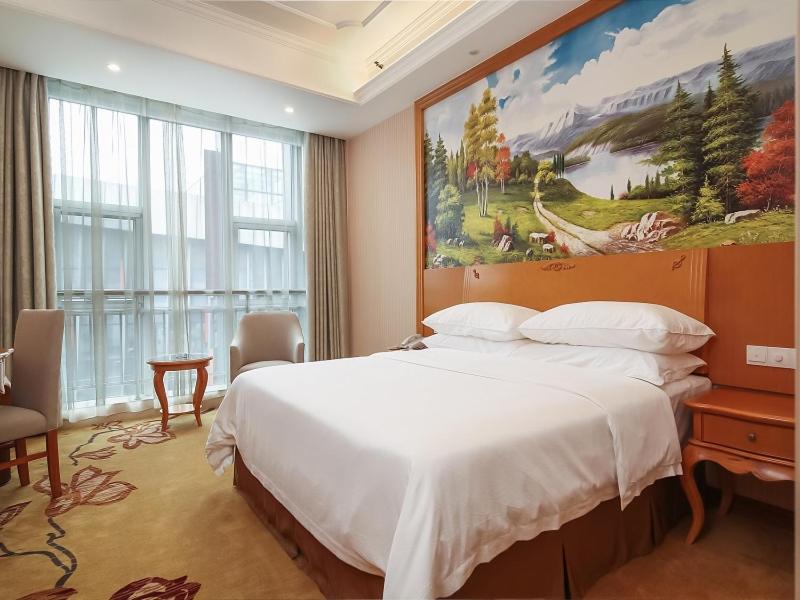 Vienna Hotel Nanjing Olympic Sports Center في نانجينغ: غرفة نوم بسرير كبير ولوحة على الحائط