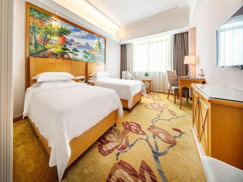 a hotel room with two beds and a large painting on the wall at Vienna Hotel Banxuegang Road in Longgang