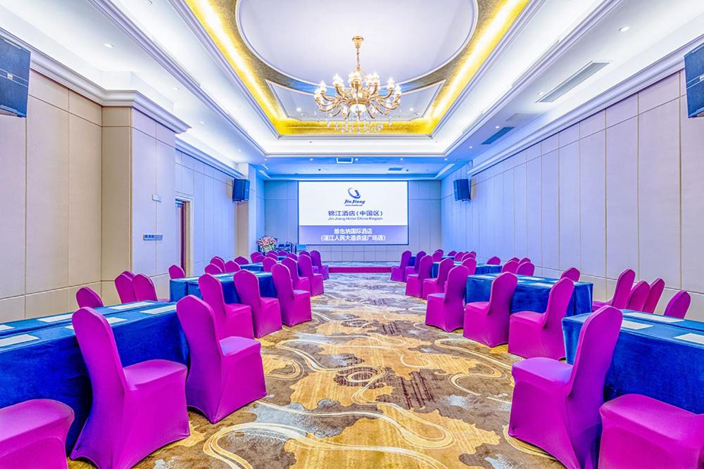 Sala de conferencias con sillas rosas y pantalla de proyección en Vienna International Hotel Guangdong Zhengjiang Renming Avenue Middle Road, en Zhanjiang