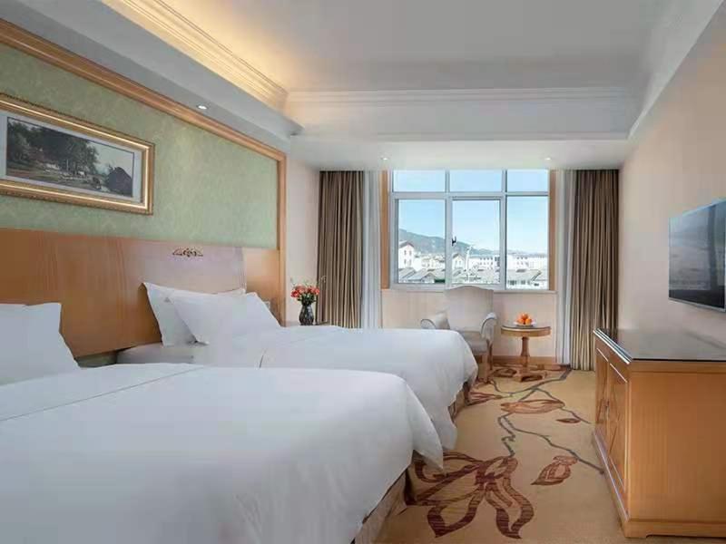 um quarto de hotel com duas camas e uma televisão de ecrã plano em Vienna International Hotel Lijiang Yuxue Avenue em Lijiang