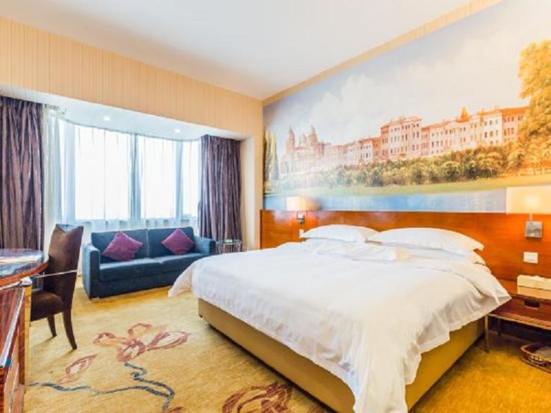 Cette chambre comprend un grand lit et un canapé. dans l'établissement Vienna International Hotel - Foshan Haiyue Branch, à Nanhai
