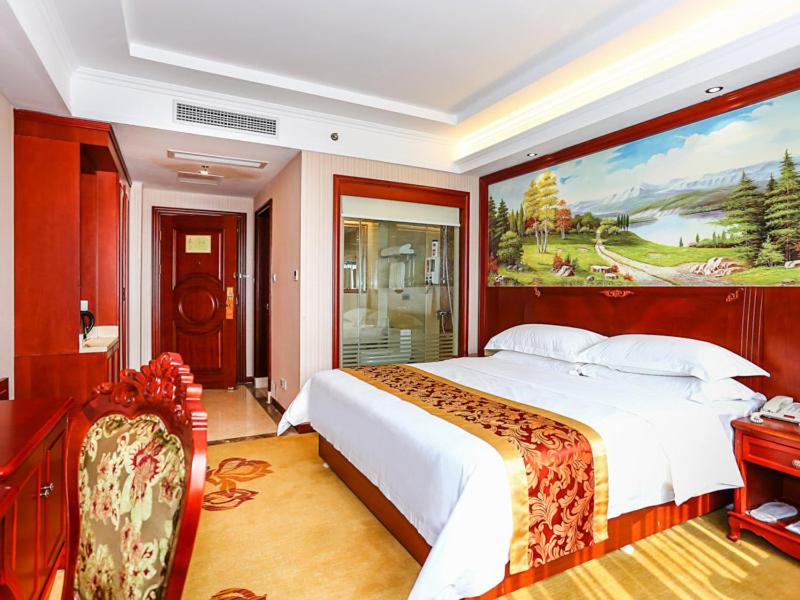 a bedroom with a large bed with a painting on the wall at Vienna International Hotel Shanghai Fengxian Nanqiao in Fengxian