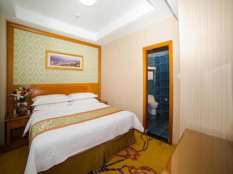 a bedroom with a large bed and a bathroom at Vienna Hotel Shandong Yantao Golden Beach Taishan Road in Yantai