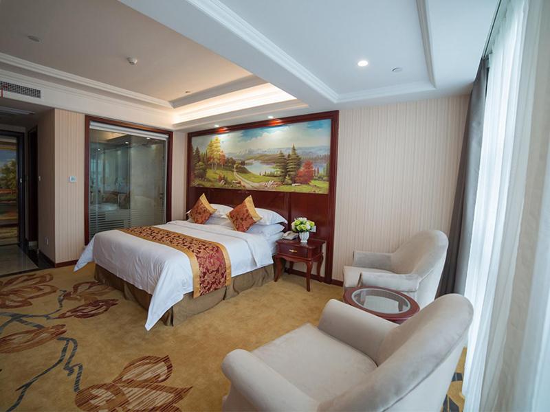 um quarto de hotel com uma cama grande e uma cadeira em Vienna Hotel Zhejiang Huzhou Changxing Mingzhu Road em Changxing