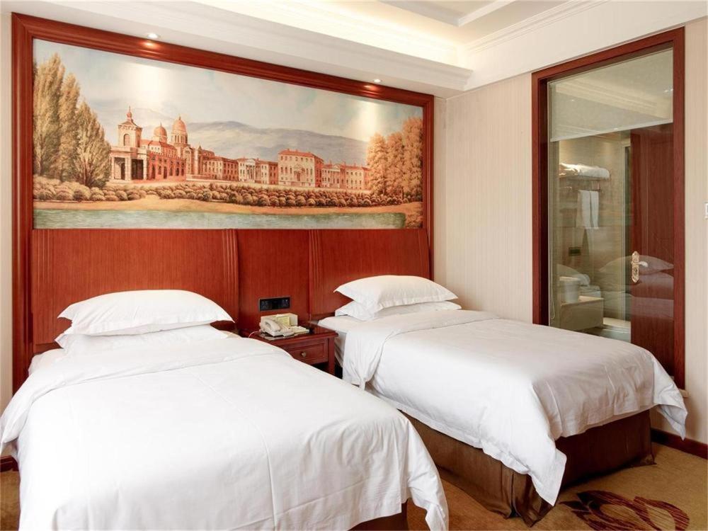 two beds in a hotel room with a painting on the wall at Vienna Hotel Jiefang East Road in Wuxi