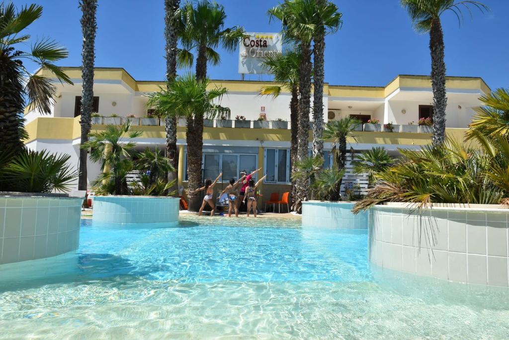 una piscina di fronte a un hotel con palme di Residence Club Costa D'Oriente a Torre dell'Orso