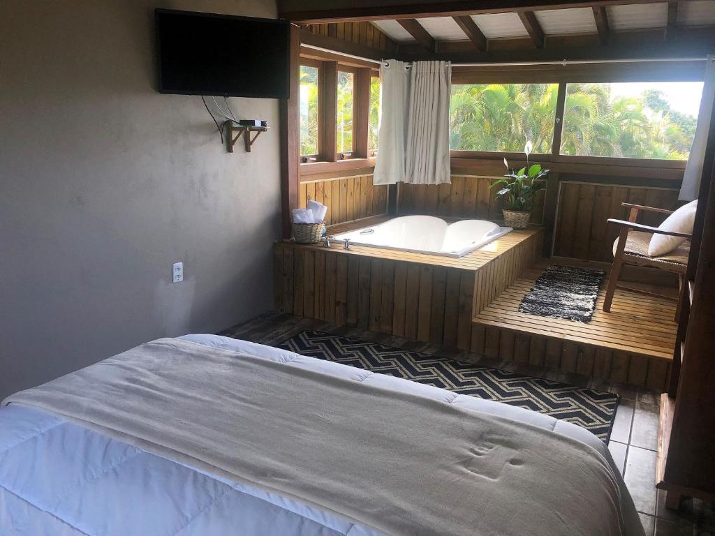 1 dormitorio con cama y ventana con bañera en Studios do Barão - Conforto e privacidade em meio à natureza en Praia do Rosa
