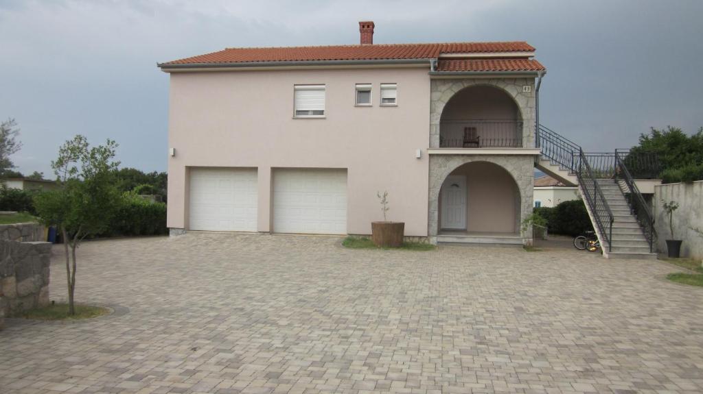 a white house with two garage doors on a driveway at Natasa apartments Krk in Vrh