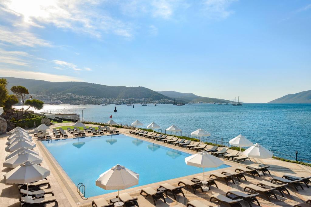 a pool with chairs and umbrellas next to the water at La Quinta by Wyndham Bodrum in Bodrum City