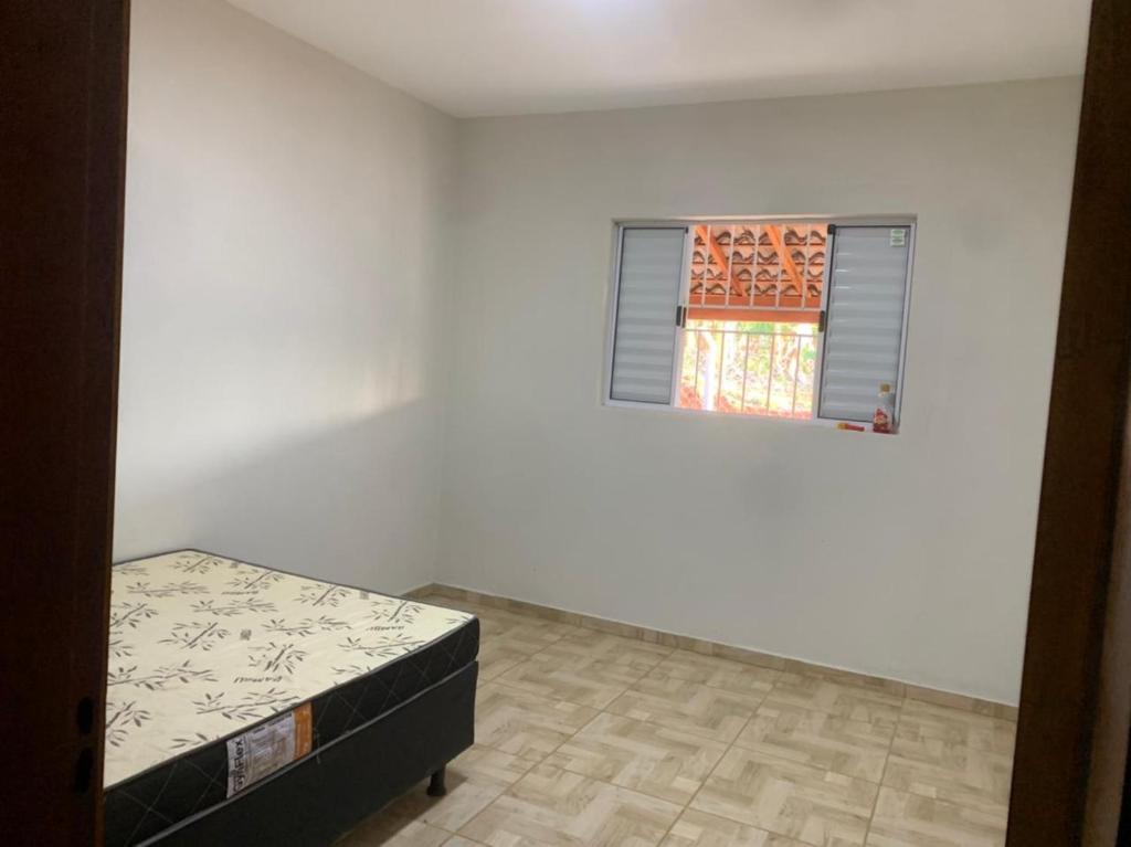 ein weißes Zimmer mit einem Bett und einem Fenster in der Unterkunft Rancho Itokazu in Delfinópolis