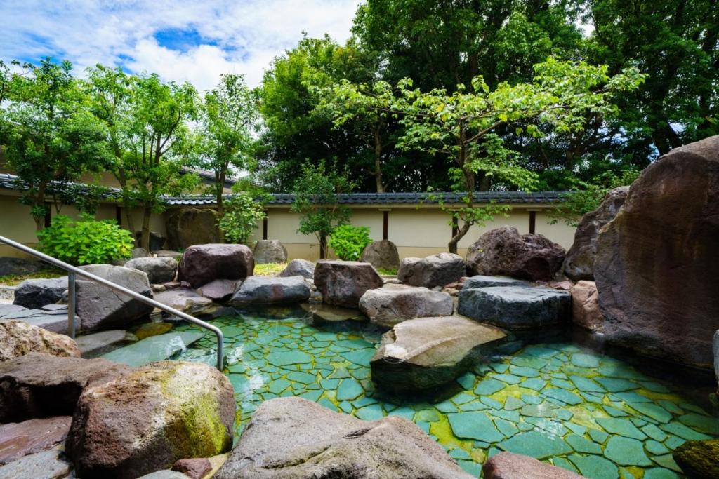 a pool of water with rocks in a garden at Hotel Beppu Pastoral in Beppu