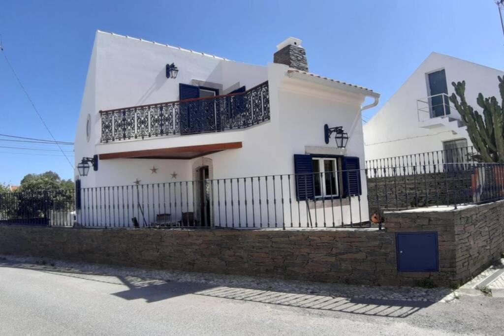 una casa blanca con persianas azules y una valla en A Casa da Foz Moradia com vista mar, en Sesimbra