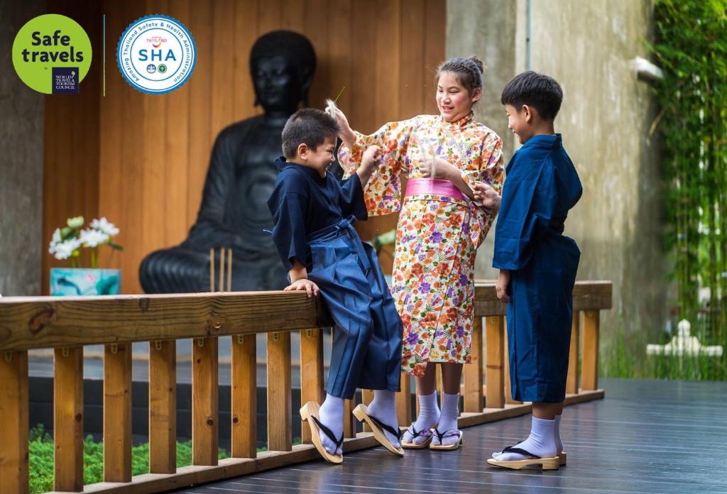 Una donna e due bambini in piedi accanto a una statua. di Zen Villa Khao Yai a Mu Si