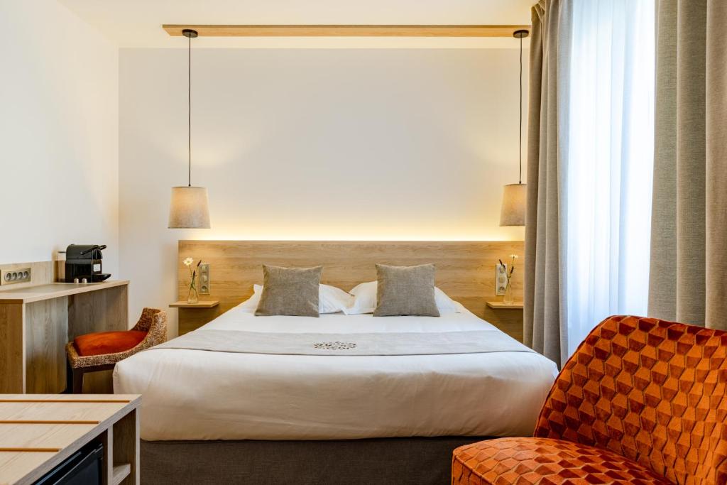 ein Hotelzimmer mit einem großen Bett und zwei Stühlen in der Unterkunft Hôtel du Lac de Madine - Maison DRAPIER in Heudicourt-sous-les-Côtes