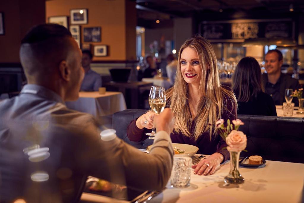 a woman sitting at a table with a glass of wine at Hotel New York by WestCord in Rotterdam