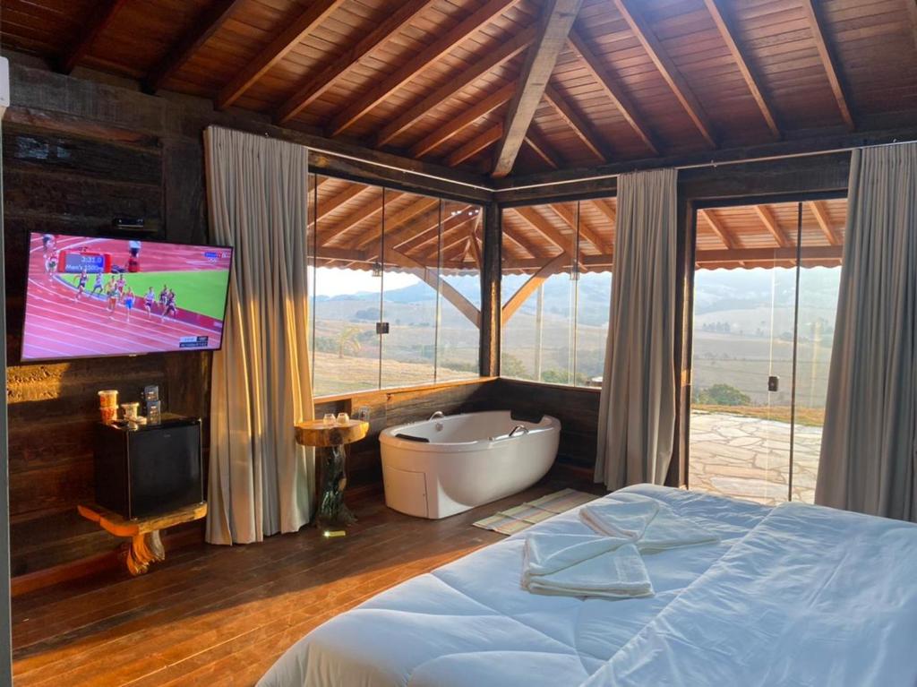 a bedroom with a tub and a tv and a bed at Pousada A Gruta in São Thomé das Letras