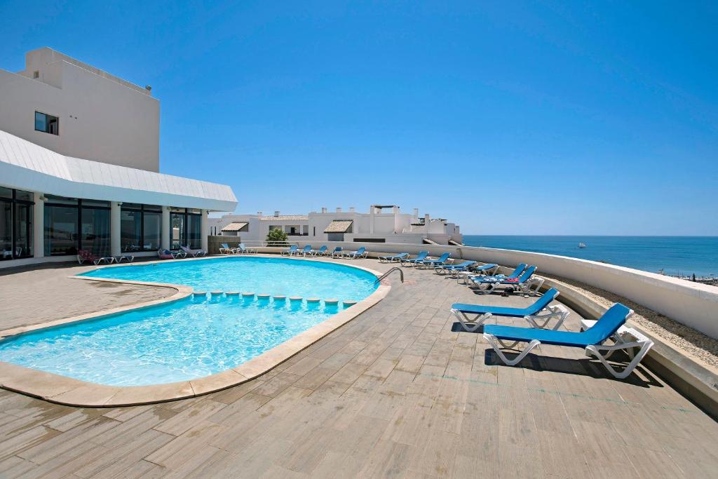 a swimming pool on a resort with chairs and the ocean at Apartamento Magnolia in Porto de Mós