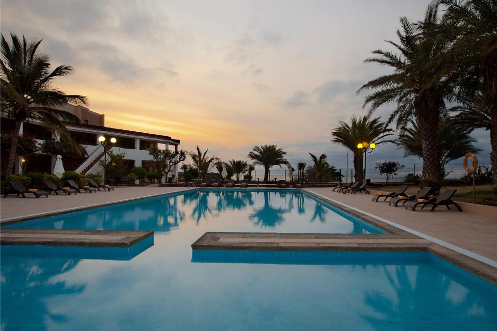 a swimming pool with a sunset in the background at Pestana Tropico Ocean & City Hotel in Praia