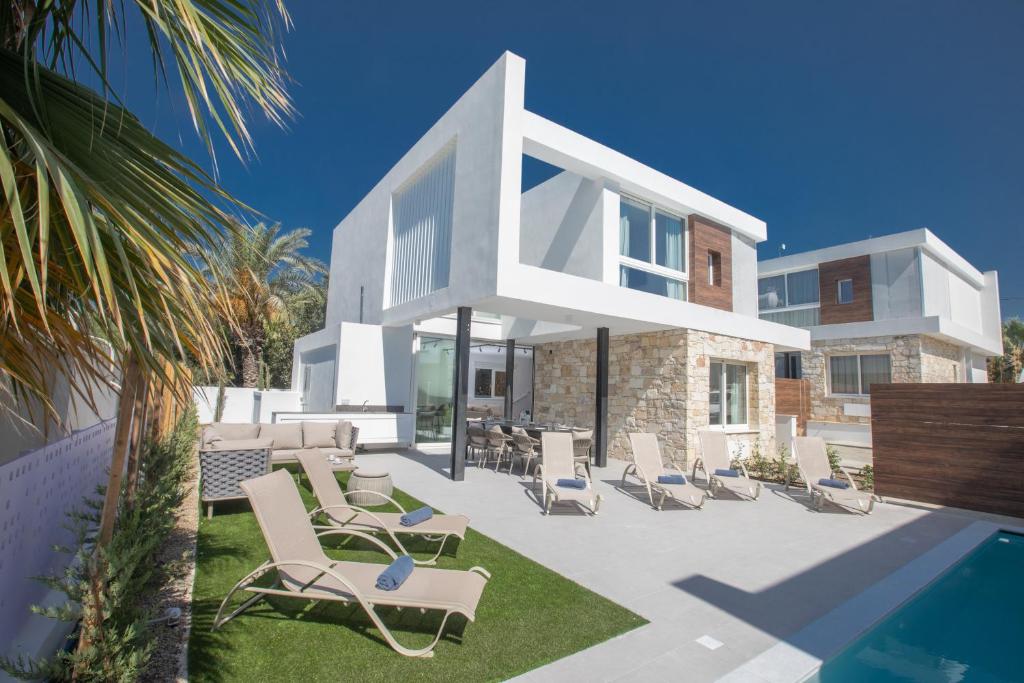 a white house with chairs and a swimming pool at Kube Luxury Villas in Ayia Napa