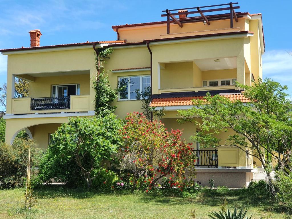 a yellow house with a balcony and some bushes at Bougenville in Kampor