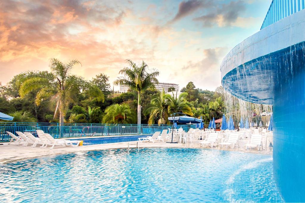 uma piscina com cadeiras brancas e um escorrega aquático em Hotel Vilage Inn All Inclusive Poços de Caldas em Poços de Caldas