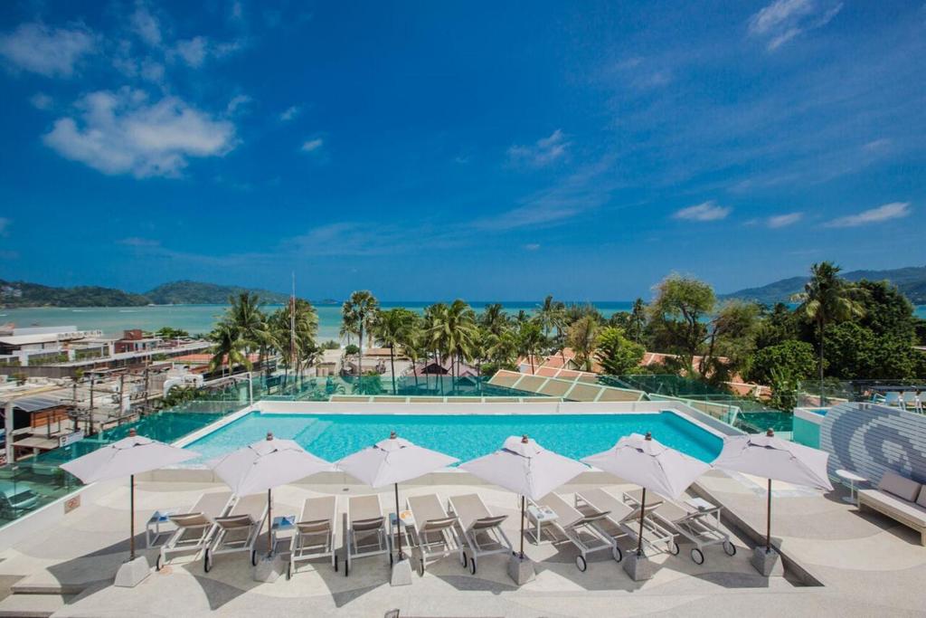 una piscina con sombrillas y sillas blancas y el océano en The Bloc Hotel - SHA Extra Plus en Patong