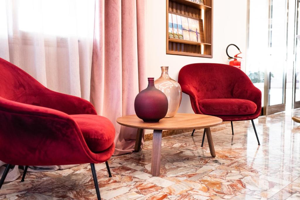 a room with two red chairs and a table with a vase at Hotel Souvenir in Lido di Jesolo