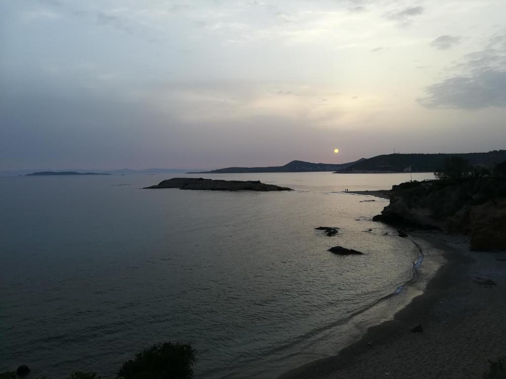 a sunset over a body of water with a beach at Studio Agia Marina Koropi in Aghia Marina