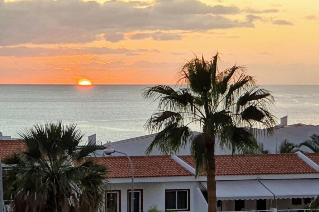 een zonsondergang boven de oceaan met palmbomen en een gebouw bij Gioiellino in Adeje