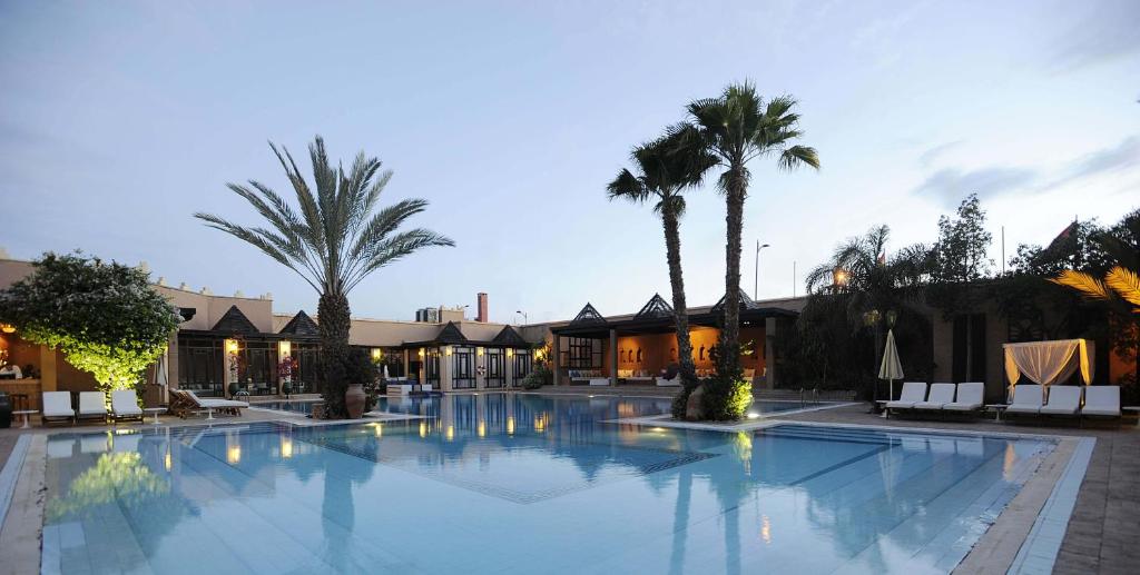 a large swimming pool with palm trees and buildings at Berbère Palace in Ouarzazate