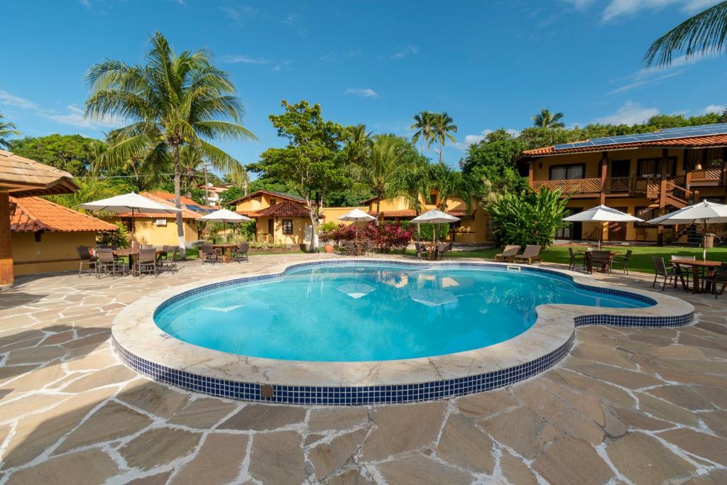 a swimming pool at a resort with tables and umbrellas at Hotel Pousada Imbassai in Imbassai
