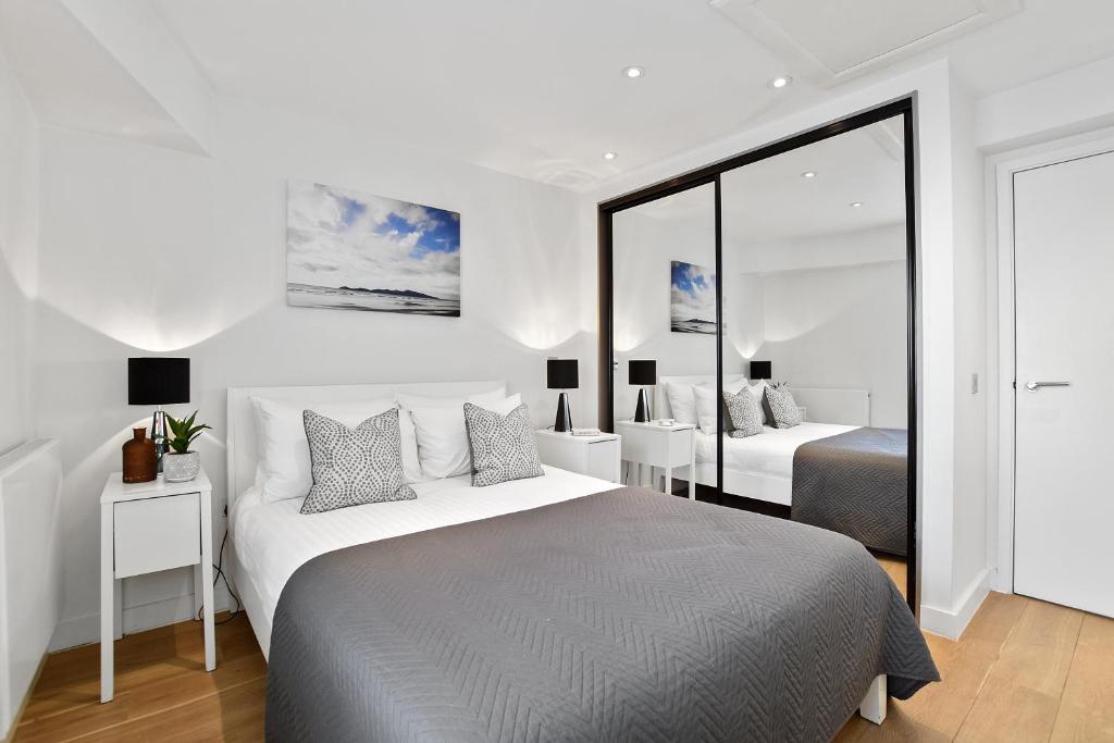 a white bedroom with two beds and a mirror at Berwick Street by Q Apartments in London