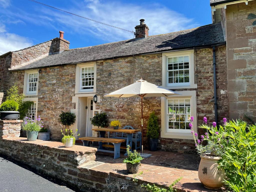 een stenen huisje met een parasol en een tafel en bank bij The Cosy Nook Cottage Company - Cosy Cottage in Warcop