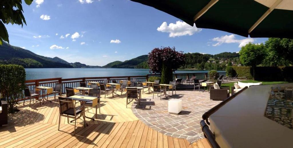 eine Terrasse mit Tischen und Stühlen neben einem See in der Unterkunft Landhotel Schützenhof in Fuschl am See