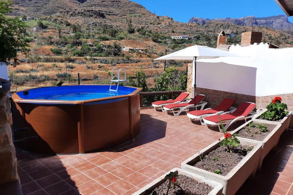 bañera de hidromasaje en un patio con sillas y sombrilla en Casa Rural Los Cipreses. Cercados de Araña, en San Bartolomé