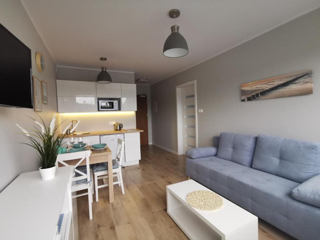 a living room with a blue couch and a kitchen at Apartament La Playa in Rowy