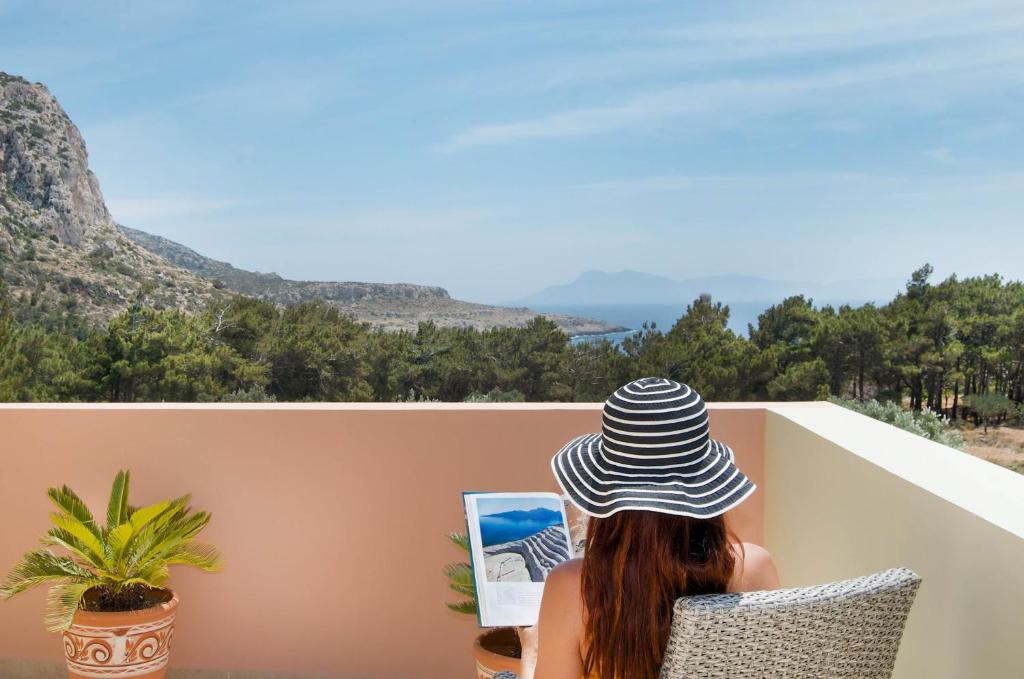 a woman in a hat sitting in a chair looking at a painting at Miraluna Aparthotel in Lefkos Karpathou