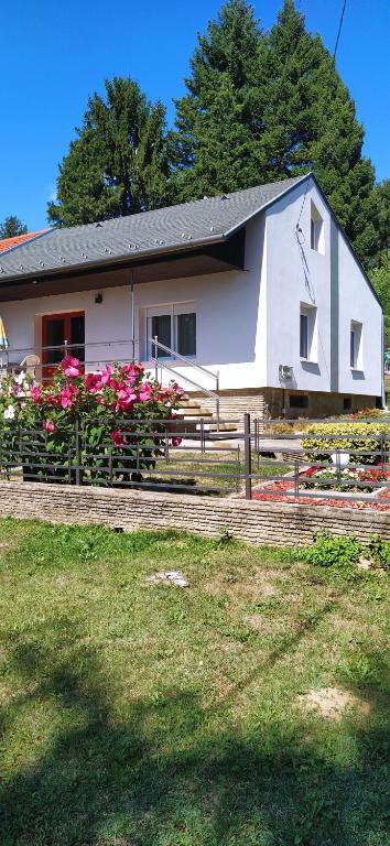 Uma casa branca com flores cor-de-rosa à frente. em Kertes nyaralóház em Keszthely