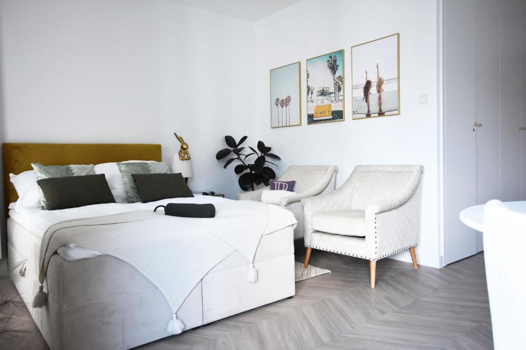 a white bedroom with a bed and a chair at Royal Sand Apartment in Gdańsk