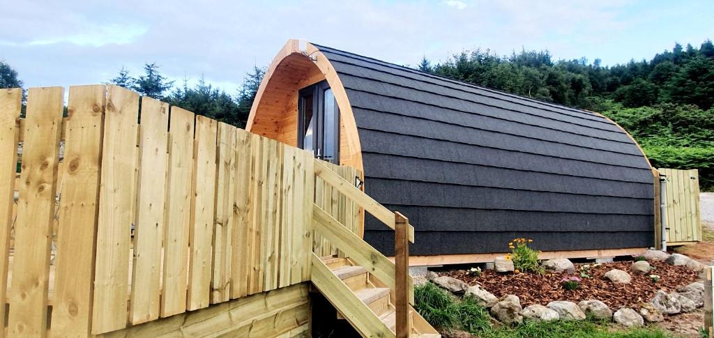 una casa con tetto nero e recinzione in legno di The Pod at Hollingwell House - Glamping NC500 Edderton a Balblair