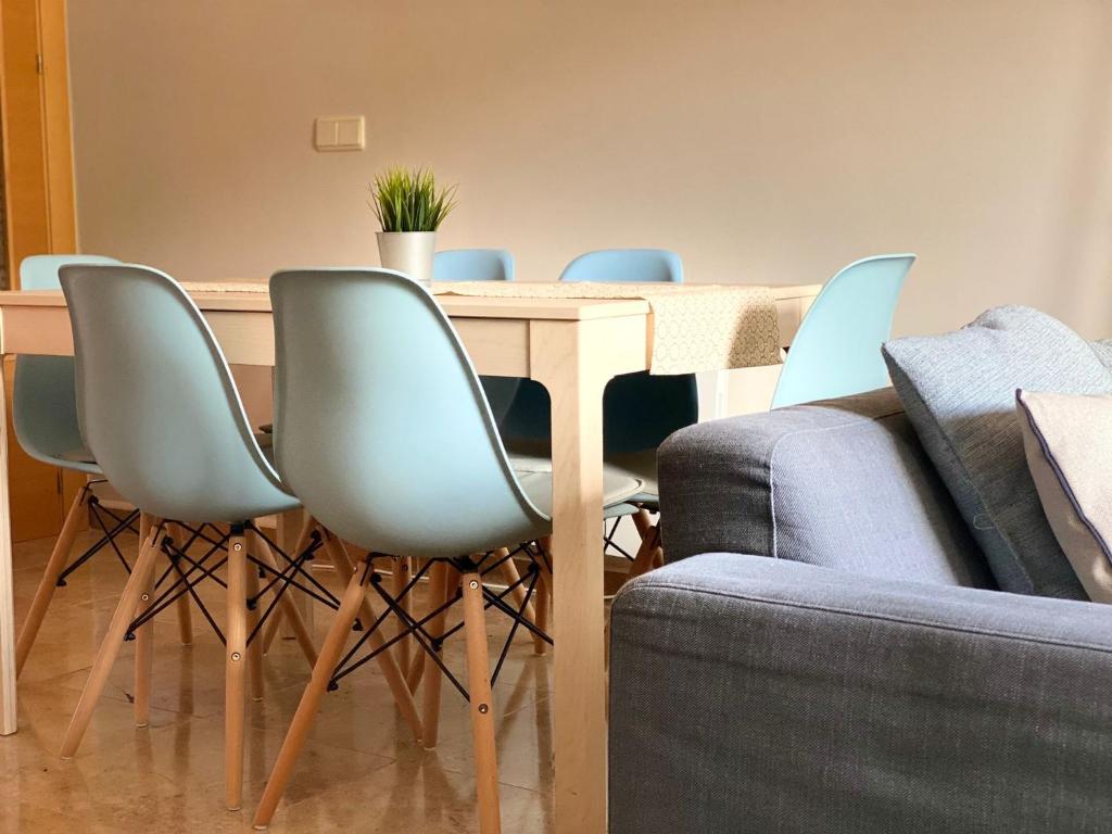 a dining room table with blue chairs and a couch at Apartamento Turístico Javalambre in Camarena de la Sierra