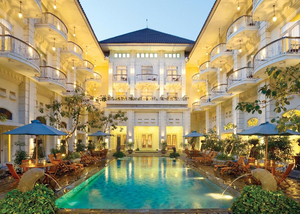 een binnenzwembad in een gebouw met tafels en parasols bij The Phoenix Hotel Yogyakarta - MGallery Collection in Yogyakarta