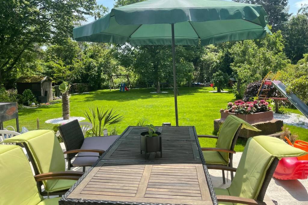 einen Holztisch mit einem grünen Sonnenschirm und Stühlen in der Unterkunft Wunderschöne Terrassenwohnung mit Blick ins Grüne! in Meerbusch