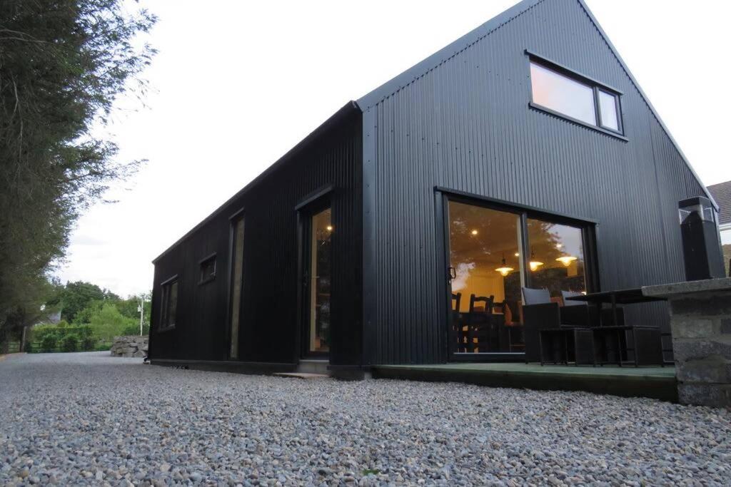 a black house with glass doors on a gravel driveway at The Boat Shed, Westport in Westport