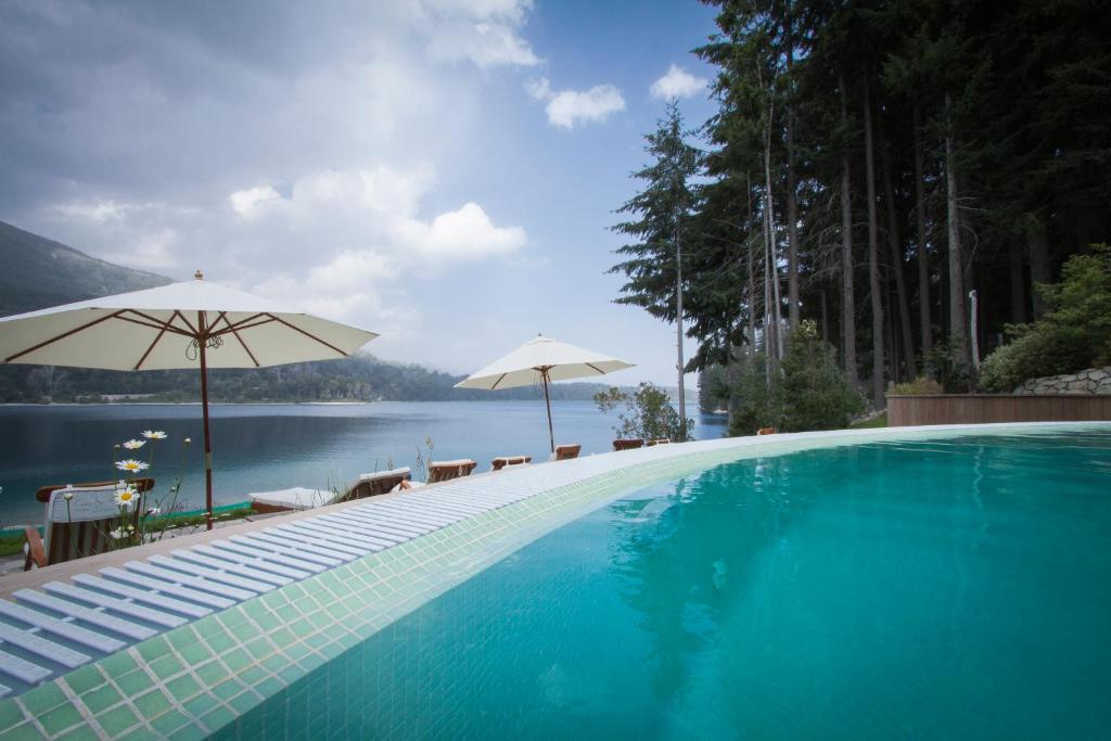 una piscina con sombrillas y un cuerpo de agua en Costa Serena Apart Cabañas & Spa en Villa La Angostura