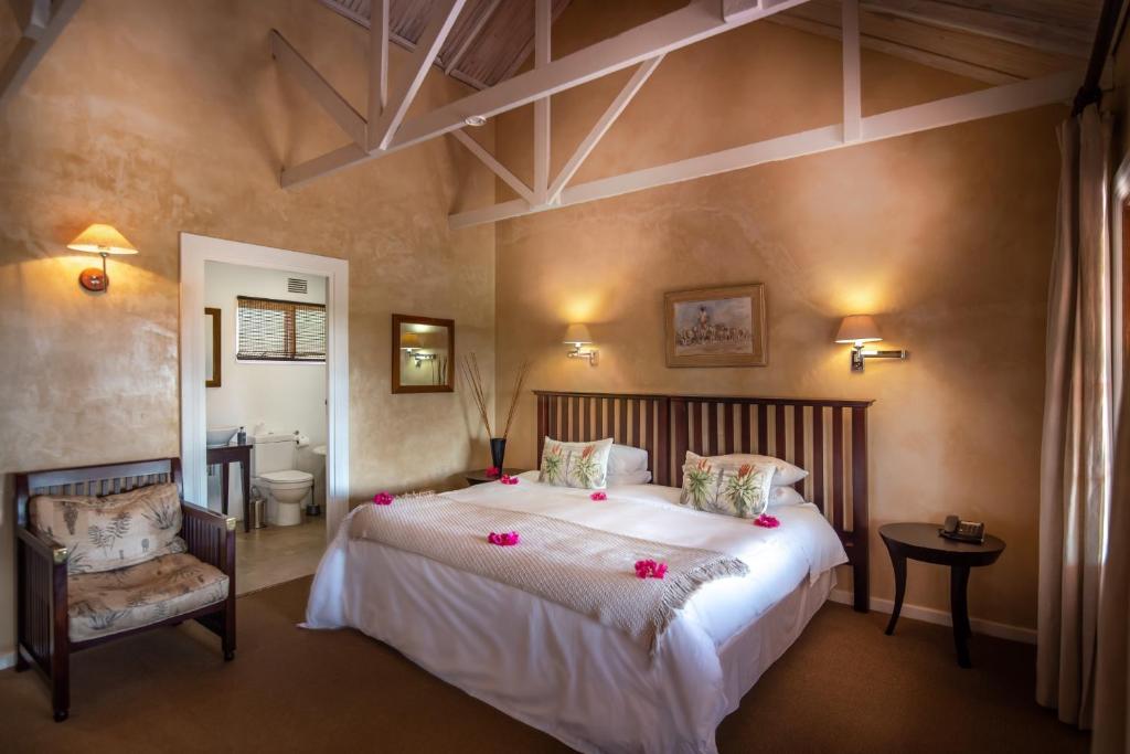 a bedroom with a large bed and a chair at Leeuwenbosch Shearers Lodge - Amakhala Game Reserve in Buyskloof